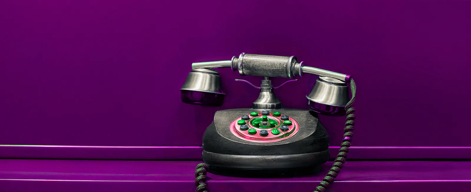 A vintage dial telephone against a purple wall